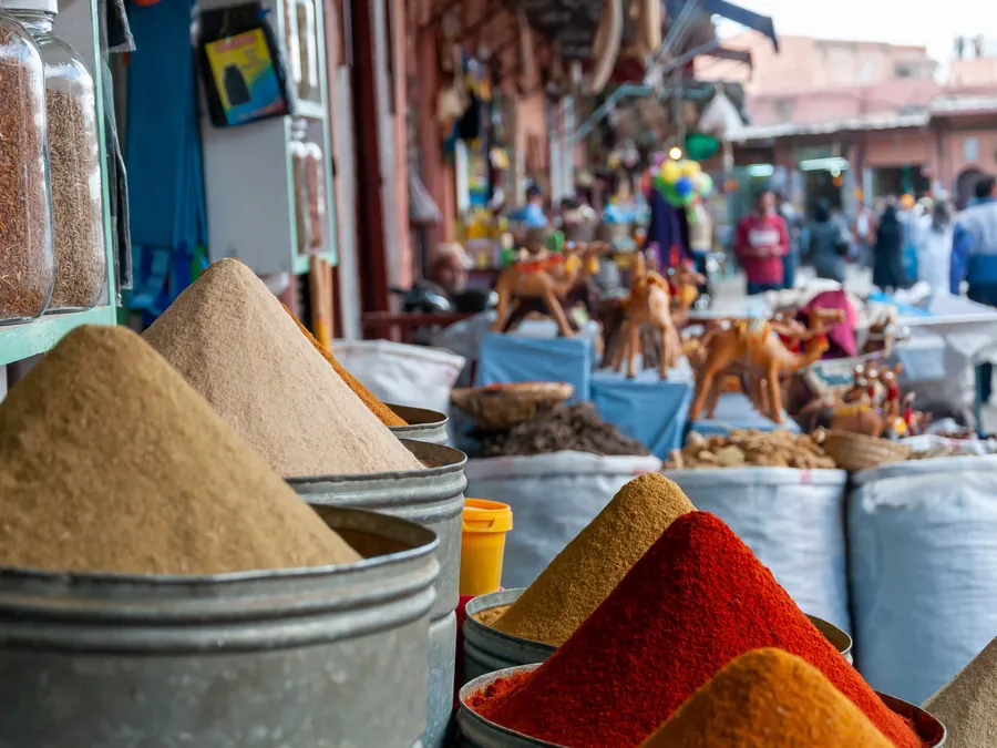 Spice stalls in a Marrakech souk, with camel figurines and shoppers in the background
