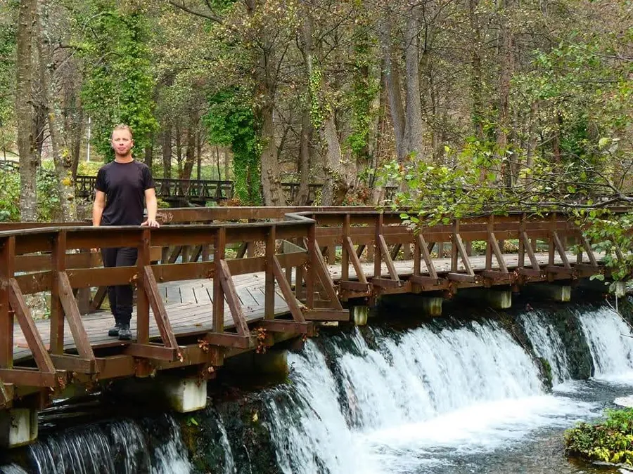Wooden boardwalk bridge over a series of cascading waterfalls in a Balkan forest park